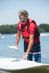 man next to a stand-up paddle board on the lake