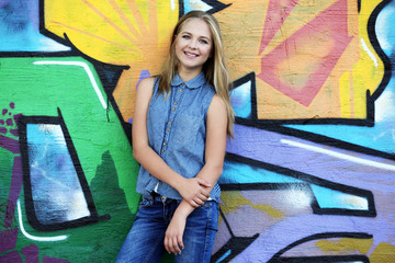 Pretty teenager girl standing near graffiti wall