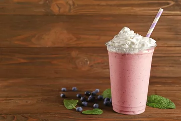 Cercles muraux Milk-shake Delicious berry milkshake in plastic cup on wooden background