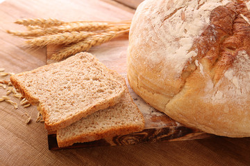 Sliced bread with wheat spikes on wooden table closeup