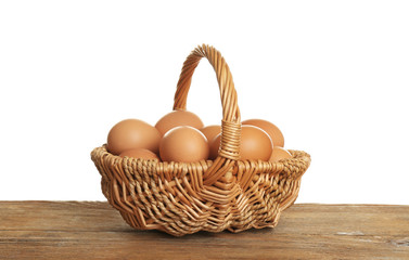 Raw eggs in wicker basket on wooden table