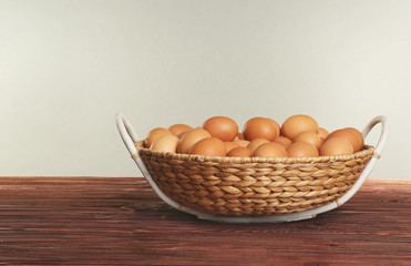 Raw eggs in wicker basket on wooden table