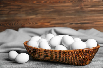 Raw eggs in basket on wooden background