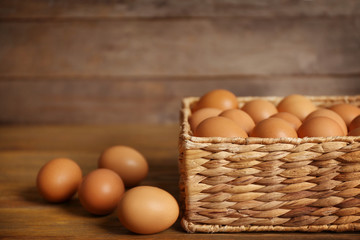 Raw eggs in basket on wooden background