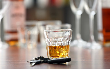 Glass with alcohol and car keys on wooden table