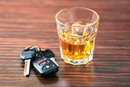 Glass with alcohol and car keys on wooden background