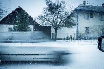 Winter Scene Through Car Window. Blurred Motion Vehicle on Street Covered with Snow. Houses on Background.