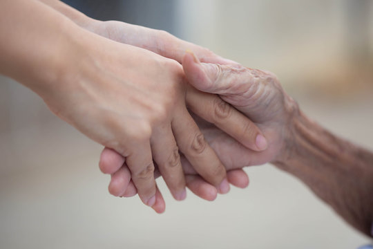 Old and young holding hands on light background, closeup