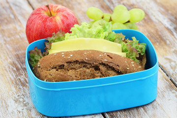 Healthy lunch box containing brown cheese roll and fresh fruit

