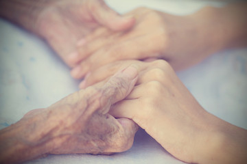 Fototapeta premium Old and young holding hands on light background, vintage tone.