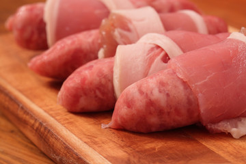 Raw sausages wrapped in bacon on a chopping board