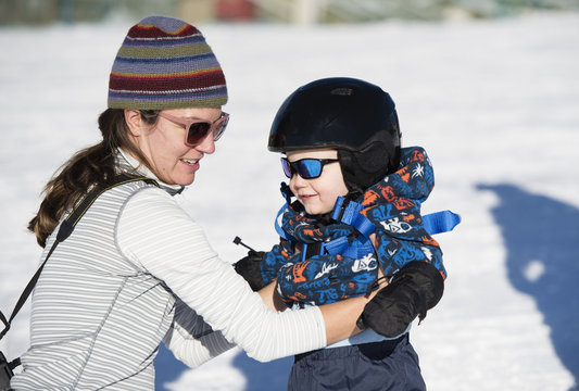 Toddler Learns to Ski at a Colorado Resort With Mom. Dressed Safely with Helmet, Sunglasses & Harness in Colorado