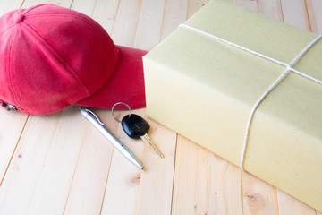 The red cap, parcel post, white paper, pen and key of car on bark table