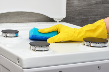 Hand in yellowglove cleaning white stove with blue sponge