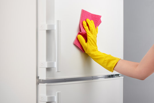 Hand in yellow glove cleaning white refrigerator with pink rag