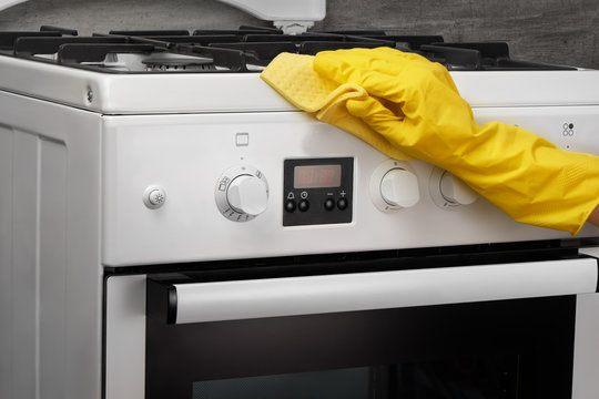 Hand in yellow glove cleaning white stove with rag
