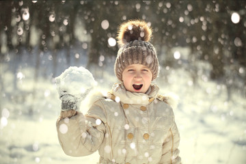 Девочка кидает снежок в зимний солнечный день. - obrazy, fototapety, plakaty