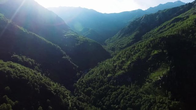 ripresa aerea panoramica tra nella valle delle montagne sopra al torrente con acqua che scorre sulle rocce, in una soleggiata giornata di estate