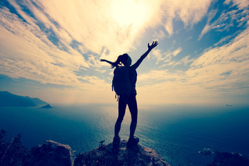 cheering young woman backpacker at seaside mountain peak