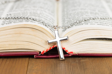 Necklace with silver cross on wooden table and opened bible book