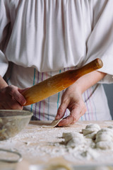 Front mid view of woman's hands making meat dumpling with wooden rolling pin.