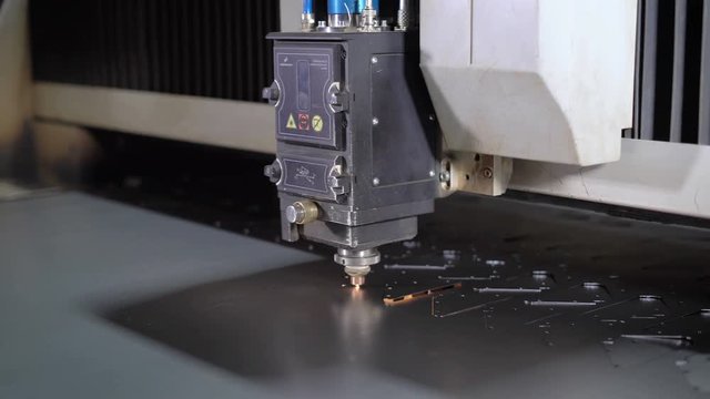 Industrial laser cutter with sparks. The programmed robot head cuts with the aid of a huge sheet of metal temperature. Modern machine improves quality and productivity.