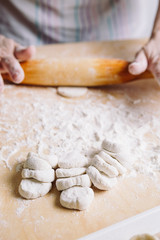 Front view of two woman's hands making meat dumpling with wooden rolling pin.