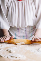 Front mid view of woman's hands making meat dumpling with wooden rolling pin.