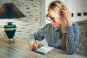 girl sitting at the table and writes in a paper notebook amounts to a list and thinking