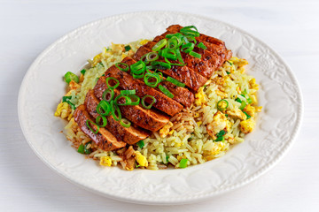 Chinese style Egg fried rice with sliced pork fillet on white wooden table.