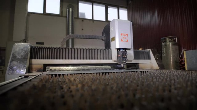 Industrial laser cutter with sparks. The programmed robot head cuts with the aid of a huge sheet of metal temperature. Modern machine improves quality and productivity.