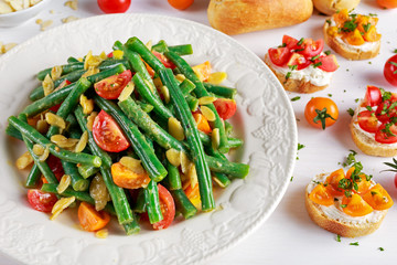 Green beans salad with Red, Yellow Tomatoes, bruschettas and flaked almond on white plate