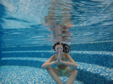 Teenage girl meditating under water in the pool. Underwater