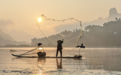 Cormorant fisherman throws a net with ancient bamboo boats at sunrise - Xingping, China - obrazy, fototapety, plakaty