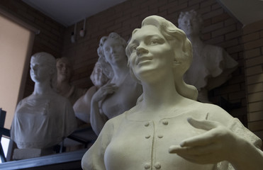 Белая скульптура женщины на фоне разных бюстов/ гипсовая скульптура и бюсты на стеллаже
