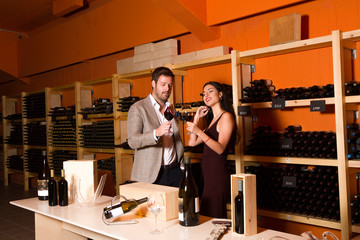 Smiling stylish young couple holding wineglasses in the winery cellar
