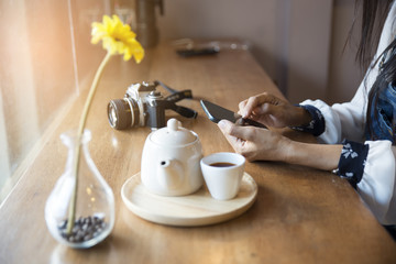 A beautiful woman using mobile phone in a cafe,old camera cup of tea, teapot and a vase of flowers on the wooden table.