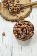 Hazelnuts in shell in brown clay bowl on a white wooden backgrou