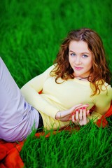 Great portrait of young charming girl in a yellow jumper with a sweet smile, resting on a green lawn in a Park on a summer day, closeup