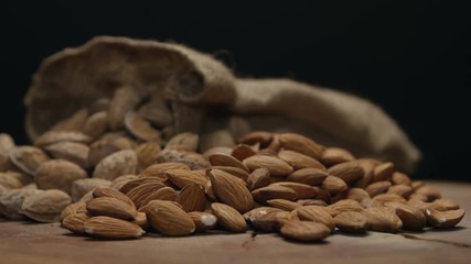 Two piles of almonds in shell and shelled on a wooden table isolated on black, rotating