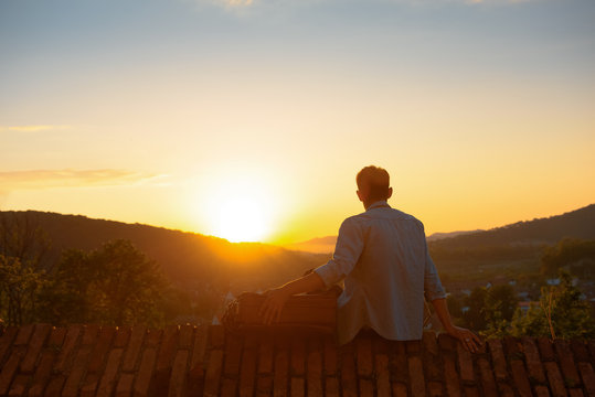 The boy who seek a new beginning. Admire the sunset sitting on  fence made of brick with luggage.