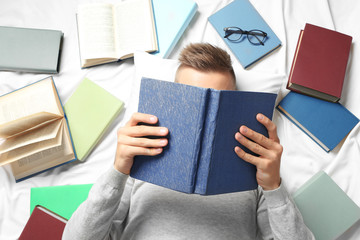 Young man reading book while lying on bed