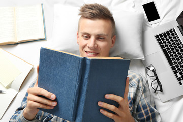 Obraz premium Handsome young man reading book while lying on bed