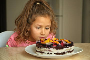 Cute little girl looking at tasty cake left on kitchen table