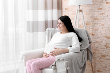 Beautiful young pregnant woman sitting on armchair at home