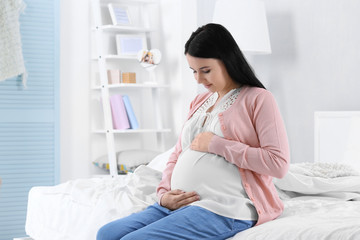 Young pregnant woman sitting on bed in cozy room