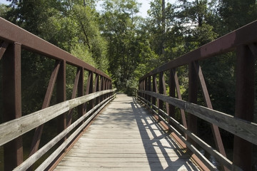Fototapeta na wymiar Wood and rusted metal bridge receding onto a wooded pathway