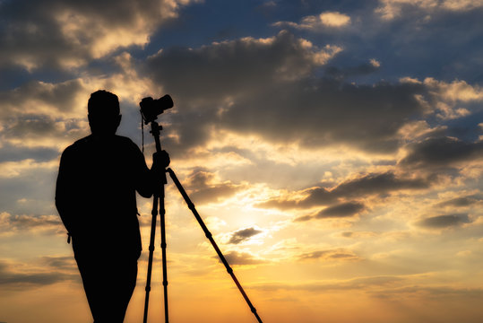 photographer silhouette with accessories and holding hand on tripod ,
taking pictures of the beautiful moments during the sunset ,sunrise