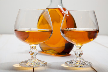 Glasses with cognac and a bottle on  white wooden background