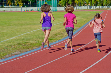 Fototapeta premium Family fitness, active mother and kids running on stadium track, back view, training with children sport concept 